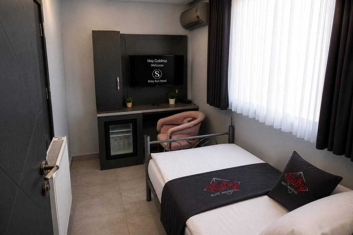 A modern hotel room with a bed, a desk with a computer, a television, and a small refrigerator.