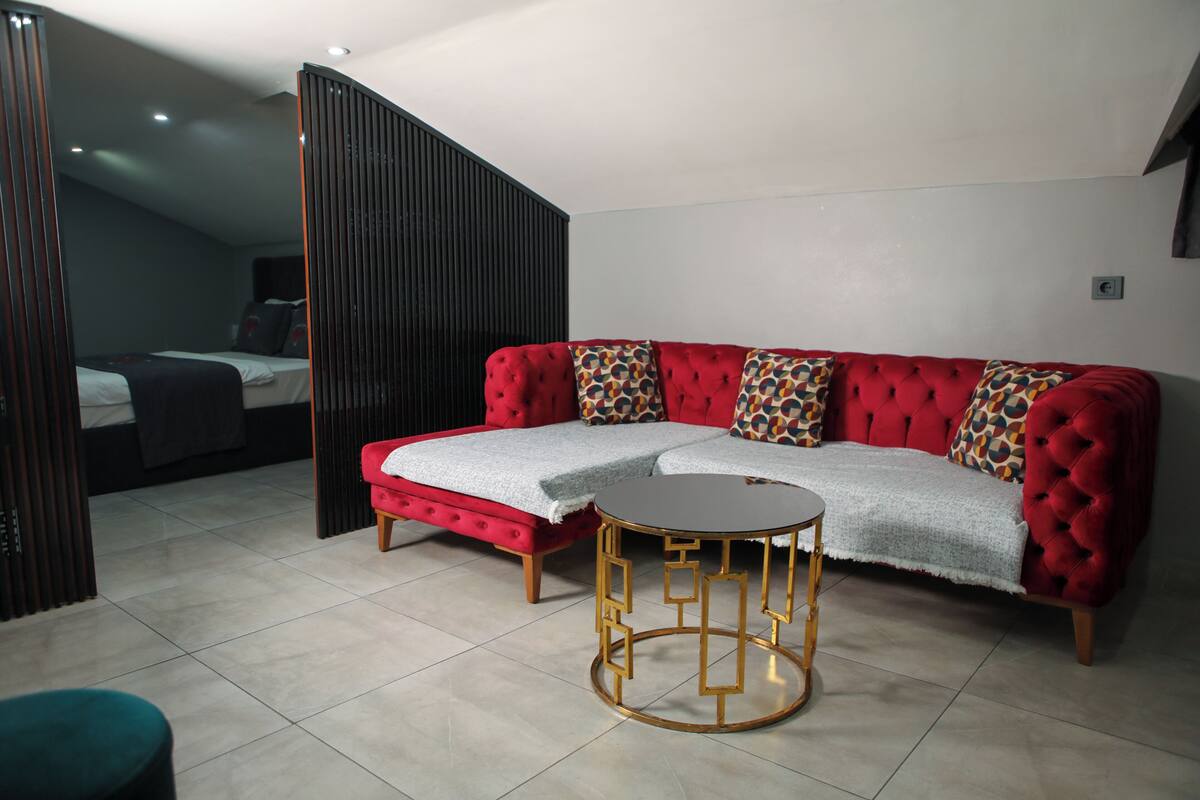 A modern living room with a red sofa, a round gold-framed table, and a bed in the background.