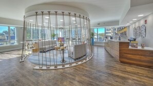 A modern reception area with a circular seating arrangement, a wooden reception desk, and large windows offering views of the outdoors. - Horizon at 77th by Elliott Beach Rentals (Myrtle Beach)