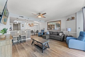 A modern living room with a sofa, coffee table, and chairs, a dining area with a table and chairs, and a kitchen in the background.