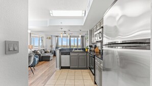 A modern kitchen with a large refrigerator, grey cabinets, and a view to the outside. - Horizon at 77th by Elliott Beach Rentals (Myrtle Beach)