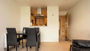 A dining area with a table and chairs, a kitchen in the background, and a leather sofa.