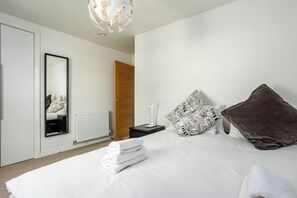 A hotel room with a bed, a bedside table, a mirror, a door, and a radiator.