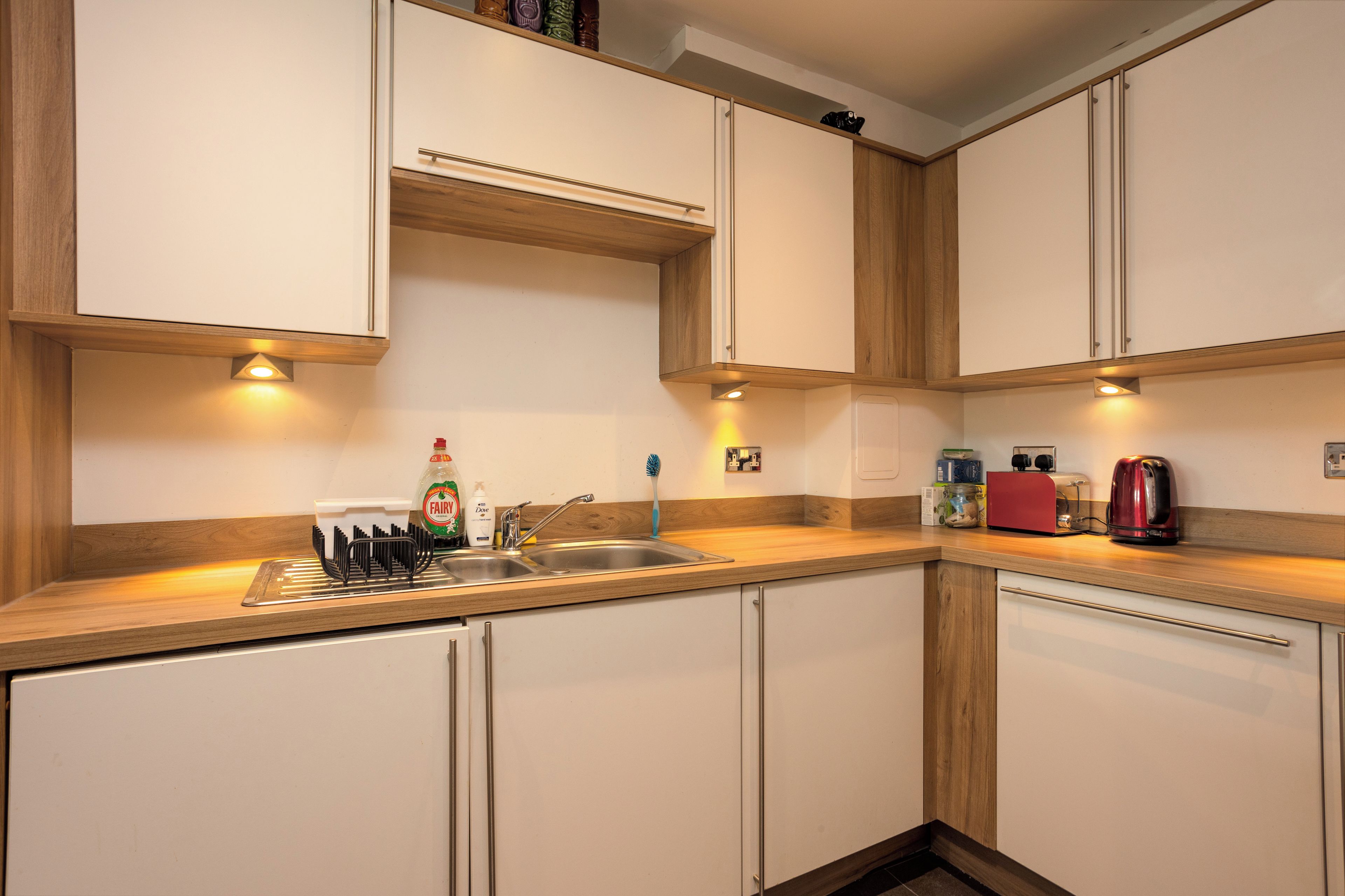 Une cuisine moderne avec des meubles blancs, un évier en acier inoxydable et un plan de travail en bois.