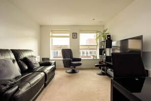 A living room with a leather sofa, a black armchair, a television, and a bookshelf. - Sleek 2BDR City Stay in the Heart of Edinburgh (Edinburgh)