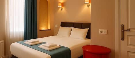 A hotel room with a bed, a red side table, and two wall-mounted lamps.