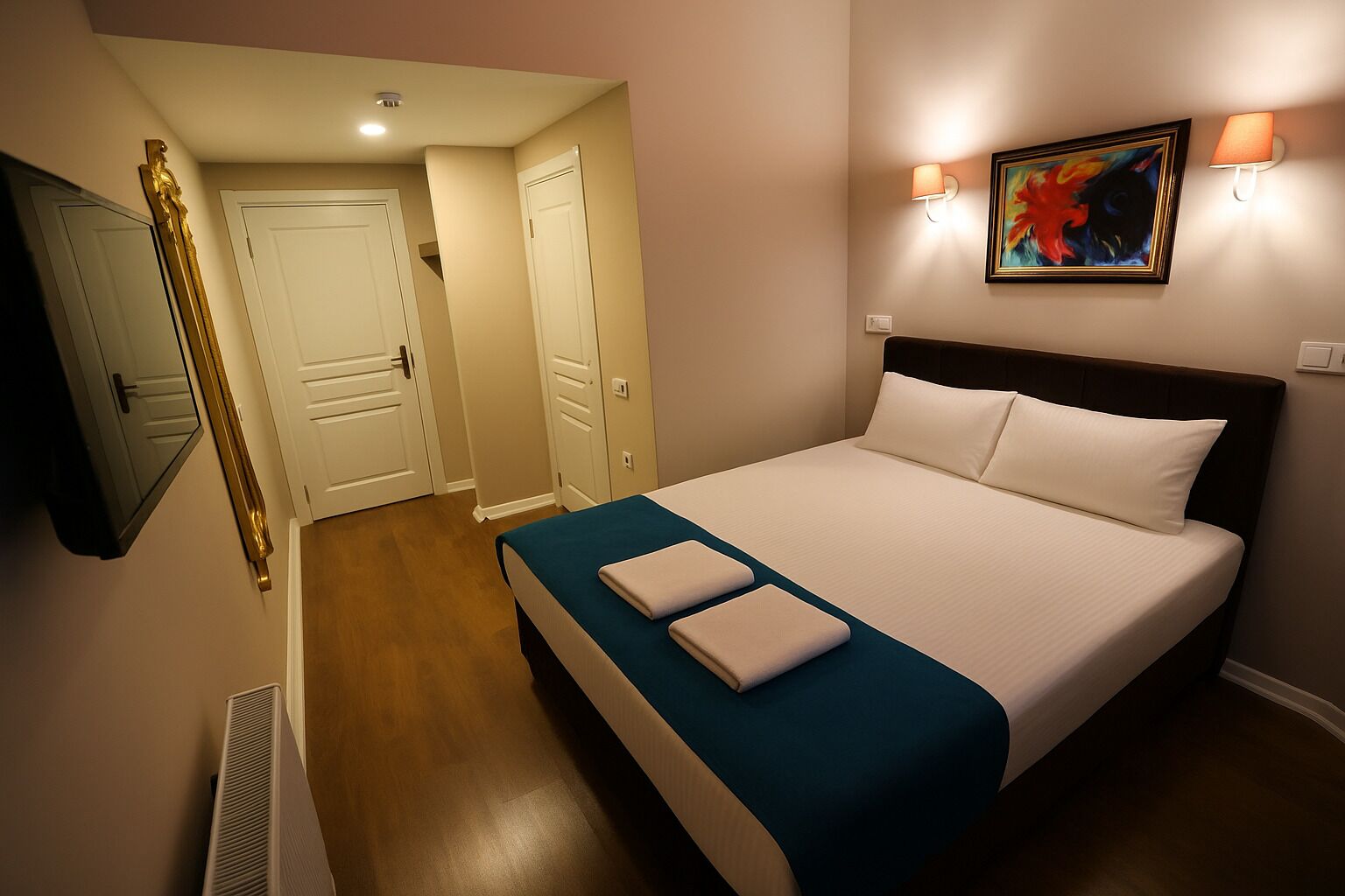 A hotel room with a bed, two bedside tables, a mirror, a painting, and a door.