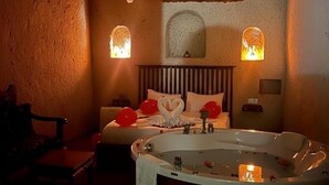 A dimly lit room with a bed, a large bathtub, and two wall-mounted lamps. - Grand Uçhisar Hotel (Nevsehir)