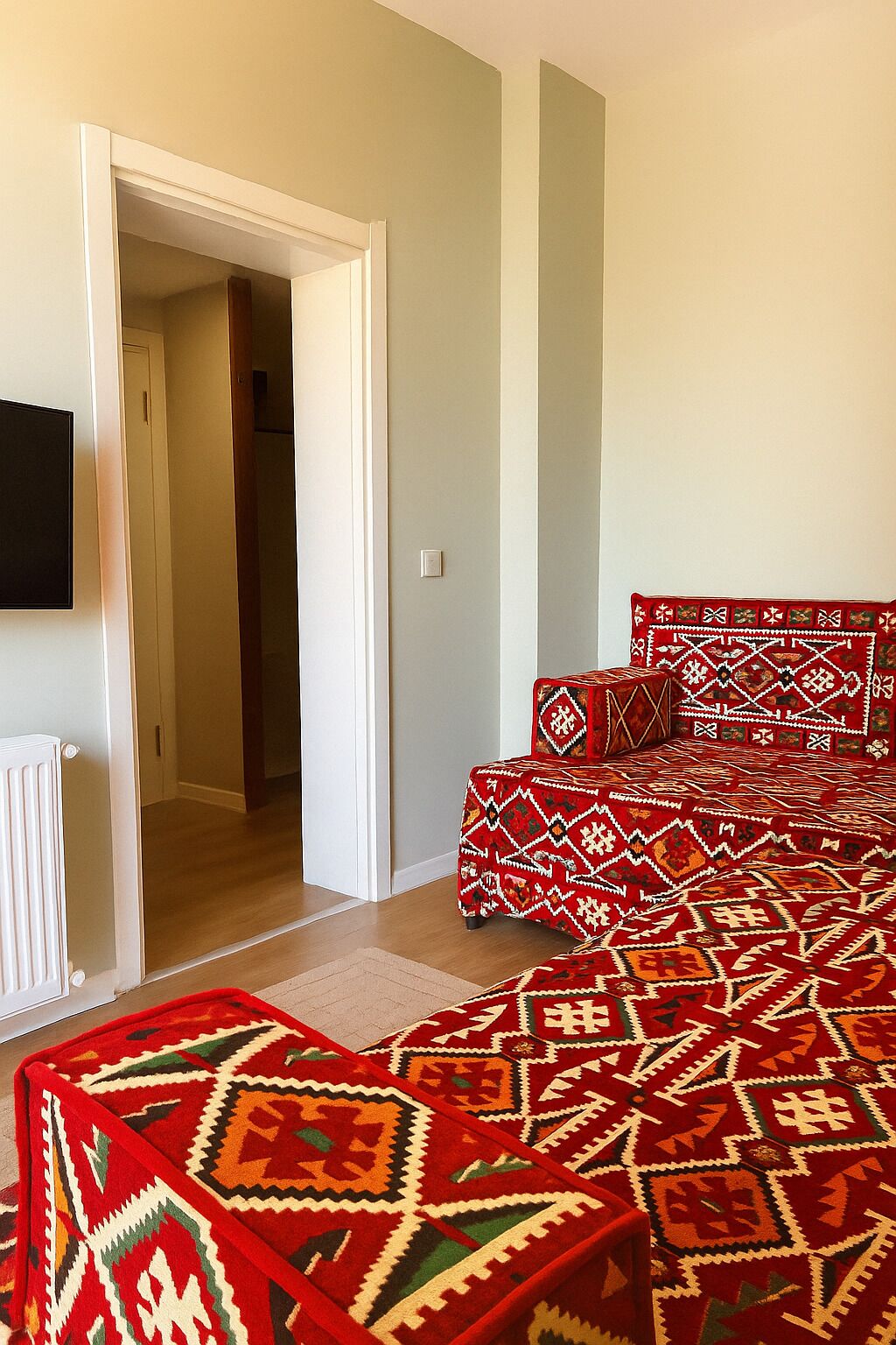 A room with a patterned red and green carpet, a white radiator, and a television mounted on the wall.