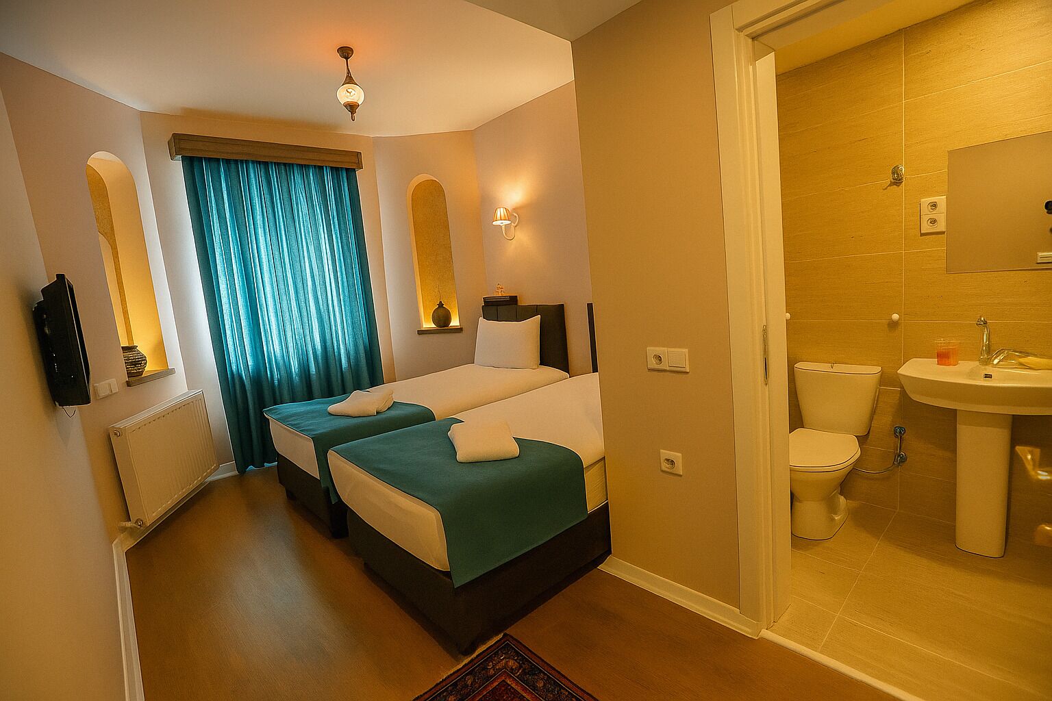 Habitació d'hotel amb dos llits, un bany amb rentapla i vàter, i una finestra petita amb cortines.