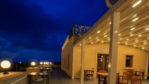 An outdoor patio area with tables and chairs, a bar, and a covered seating area with a view of the sky. - Grand Uçhisar Hotel (Nevsehir)