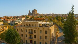 The Grand Uchisar Hotel with a rooftop terrace, a red carpet entrance, and a view of the cityscape and a prominent rock formation in the background. - Grand Uçhisar Hotel (Nevsehir)