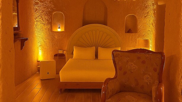 A bedroom with a bed, a chair, a nightstand, and a lamp. - Grand Uçhisar Hotel (Nevsehir)