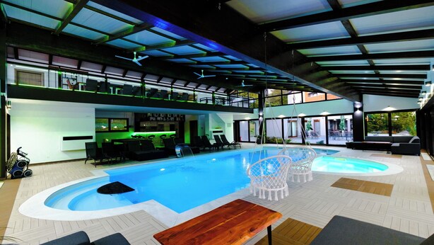 An indoor swimming pool with a wooden bench, lounge chairs, and a bar area. - Apartment, 4BDR, shared pool (Sarajevo)