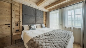 Une chambre avec un plafond en bois, un grand lit recouvert d’une couette grise et une fenêtre avec des rideaux.