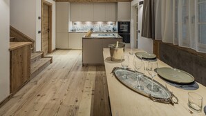 Une cuisine moderne avec un plancher en bois, un îlot central et un coin repas agrémenté d’un plateau et de verres.