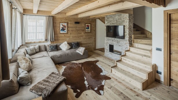 Un salon moderne avec un grand canapé d’angle, une cheminée en pierre, un escalier en bois et un tapis en peau de vache.