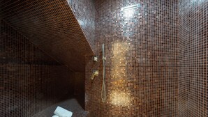 Une salle de bain carrelée avec un espace douche, un porte-serviettes et une pomme de douche visible.