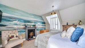 Ein Schlafzimmer mit einem großen Gemälde, einem Kamin, einem Bett mit Kissen und einem Sessel.