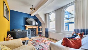 Ein Wohnzimmer mit Kamin, Fernseher, großem Fenster und einem gemusterten Teppich.