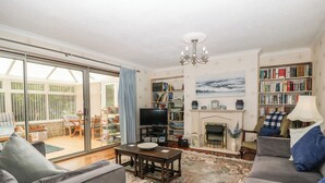 A living room with a fireplace, bookshelves, a television, and a dining area with outdoor seating. - Melita (Langport)