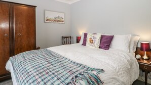 A bedroom with a large bed, a wooden wardrobe, a chandelier, and a framed picture on the wall. - Melita (Langport)