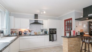 A modern kitchen with white cabinets, a black stove, and a brick island. - Melita (Langport)