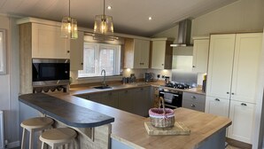 A modern kitchen with a central island, stainless steel appliances, and pendant lighting. - Yorkshire View Lodge (York)