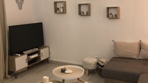 Una sala de estar moderna con una televisión de pantalla plana, un sofá, dos pequeñas mesitas auxiliares y tres estanterías montadas en la pared con objetos decorativos.