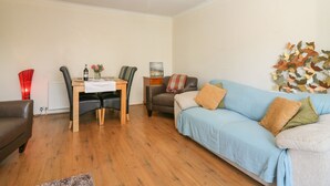 A cozy living room with a wooden dining table, two chairs, a blue sofa, and a decorative wall piece. - Blue Skies Cottage (Arbroath)