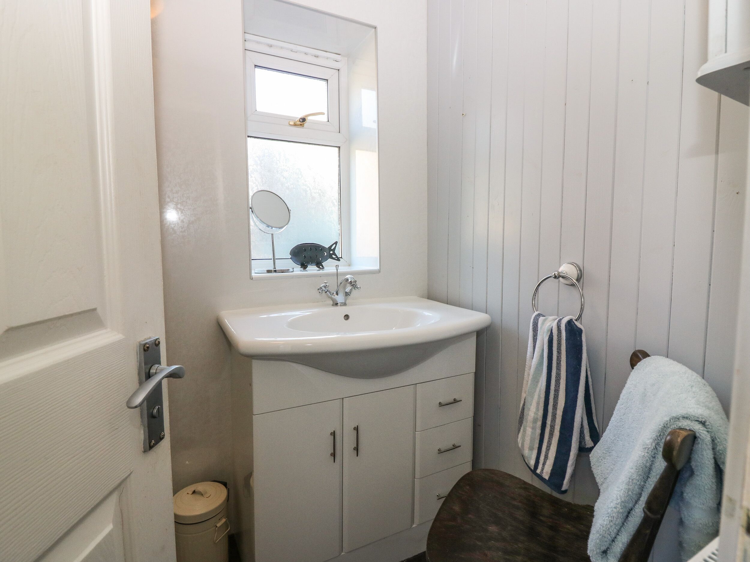 Une petite salle de bain avec un lavabo blanc, un miroir au-dessus et un porte-serviettes sur lequel est posée une serviette à rayures.