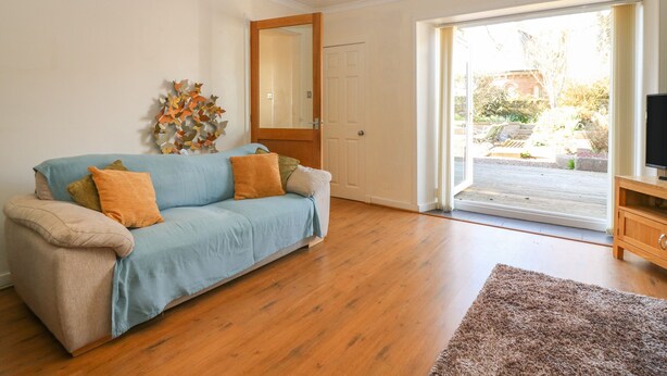 A living room with a light blue sofa, wooden flooring, a mirror, and a television on a wooden stand. - Blue Skies Cottage (Arbroath)