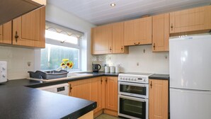 A kitchen with wooden cabinets, a black countertop, a stove, an oven, and a refrigerator. - Blue Skies Cottage (Arbroath)