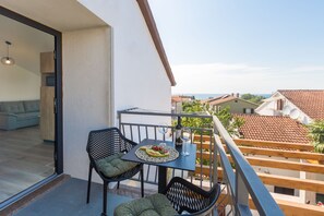 A balcony with a table set for two, a sofa, and a view of the sea and neighboring buildings. - 250 m from the beach, modern, air-conditioned, sleeps 2 to 3 people (Porec)