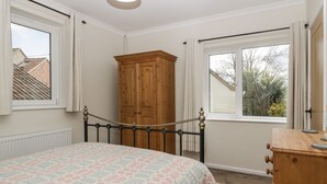 A bedroom with a bed, a wooden wardrobe, a dresser, and two windows with curtains. - Long Batch Cottage (Shepton Mallet)
