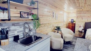 A cozy cabin-style interior with a kitchen area featuring a sink, countertop, and knife block. There are two chairs and a small table with a plant. - Lake Victoria, Yellow Cabin , Panoramic views overlooking the lake (Alexandria)