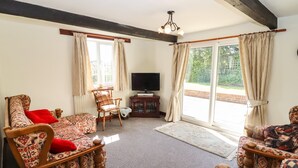 A living room with a sofa, armchair, and a television. There is a window with curtains and a view of greenery outside. - The Vinery (Gloucester)
