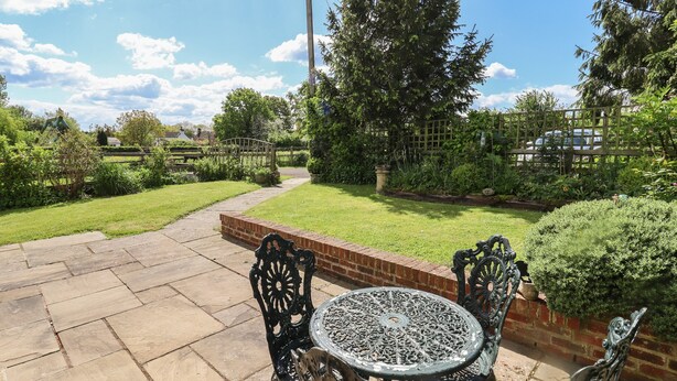 A patio with a round table and two chairs, surrounded by a brick wall and a garden with a wooden fence. - The Vinery (Gloucester)