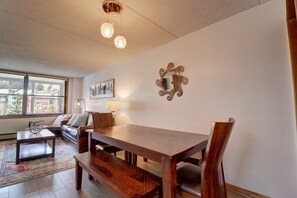 Een eetgedeelte met een houten tafel en banken, een bank en een lamp.