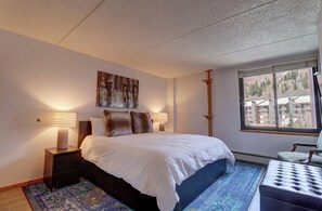 Een slaapkamer met een bed, bedlampjes, een raam met uitzicht en een decoratief wandobject.