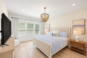 A bedroom with a bed, bedside tables, a TV, and a window with blinds.