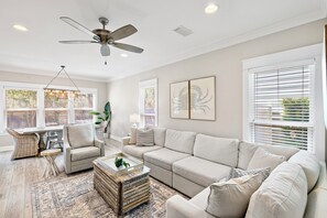 A spacious living room with a ceiling fan, a large sofa, a coffee table, and a patterned rug. - ☀️ GOLF CART, HEATED POOL, Private Hot Tub, Bikes, Ping-Pong, Walk to Rosemary (Inlet Beach)