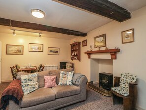 A cozy living room with a sofa, a fireplace, and a dining area with chairs and a table. - Dollar Ward House Basement (Cirencester)