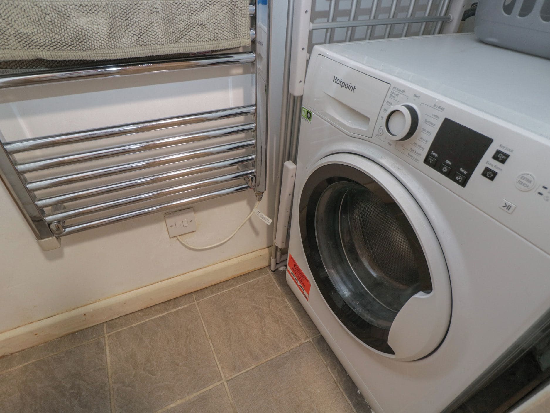 A front-loading washing machine with a control panel, a metal drying rack, and a power outlet.