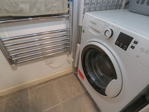 A front-loading washing machine with a control panel, a metal drying rack, and a power outlet.