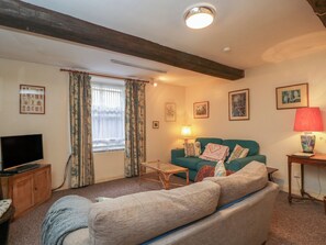 A living room with a sofa, a television, a lamp, and artwork on the walls. - Dollar Ward House Basement (Cirencester)