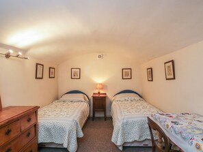 A small, cozy bedroom with two single beds, a wooden dresser, and a small table with a lamp. - Dollar Ward House Basement (Cirencester)