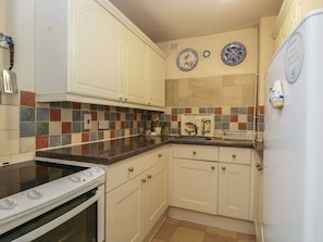 A kitchen with white cabinets, a stove, and a refrigerator. There are colorful tiles on the backsplash and two decorative plates on the wall.