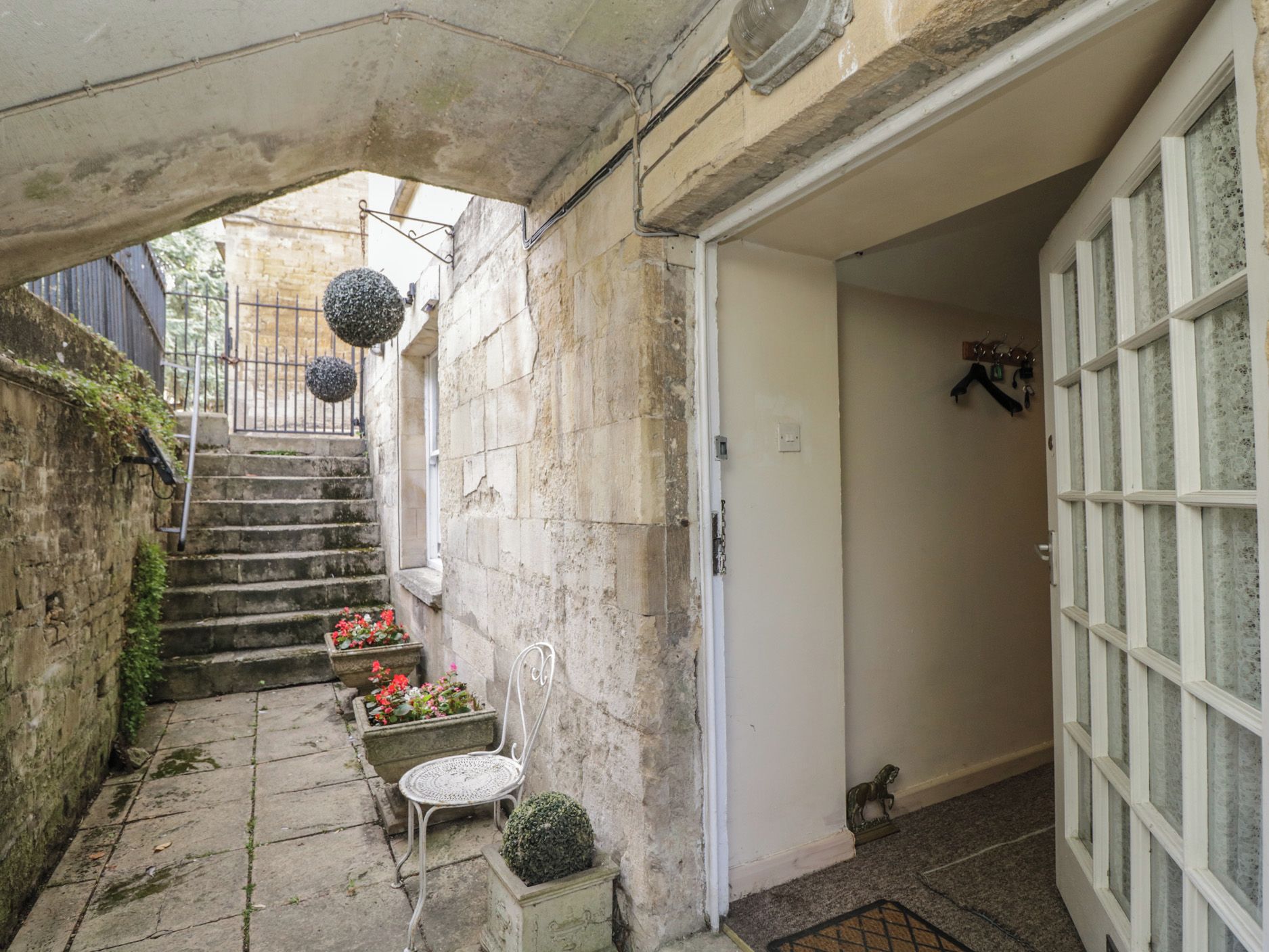 A narrow stone staircase leading to a door, with a small table and potted plants at the bottom.