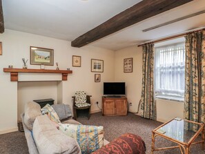 A living room with a sofa, a television, a small table, and a window with curtains.